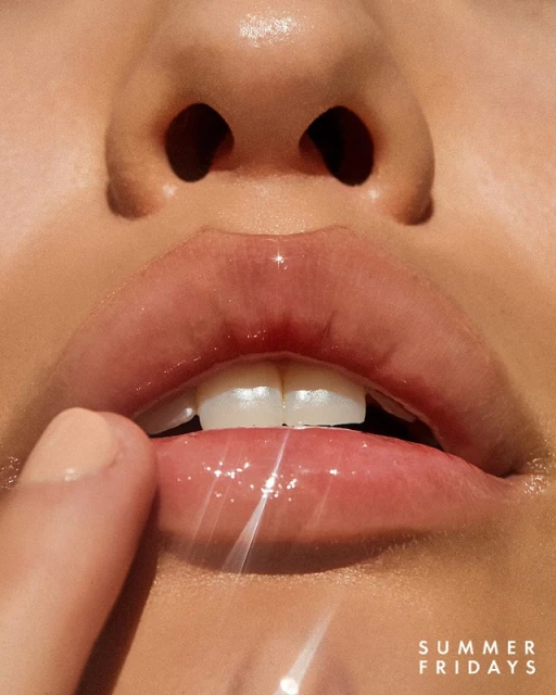 Close-up of a woman's face features; full lips, teeth, and finger touching lip. Soft lighting, glossy lips, beauty shot, minimal background.
