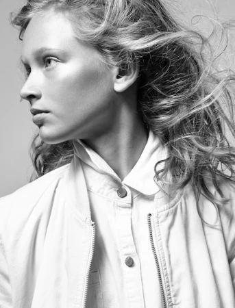 Black and white portrait of a young woman with windswept hair wearing a collared button-up shirt and jacket