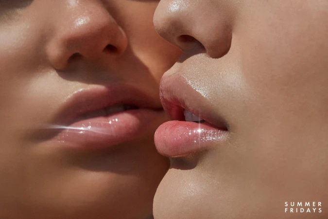Close-up of two adult female faces with glossy lips and soft skin, featuring cosmetic product and skincare brand SUMMER FRIDAYS.