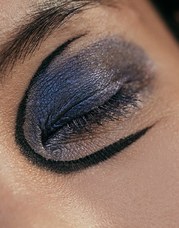 Close-up macro shot of a closed eye featuring shimmering purple eyeshadow and sharp black graphic eyeliner by Jen Fiamengo.