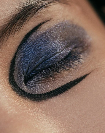 Close-up macro shot of a closed eye featuring shimmering purple eyeshadow and sharp black graphic eyeliner by Jen Fiamengo.