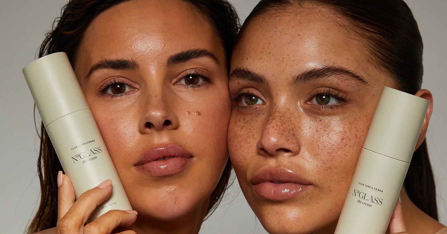 Close-up of two diverse women holding skincare bottles, emphasizing natural beauty, cosmetic product, and minimalist studio setting.