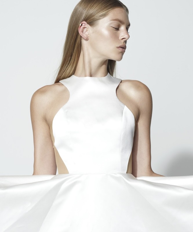 Blonde woman in a white dress with high neck poses in a studio with a white background. The dress features a fitted bodice and full skirt.