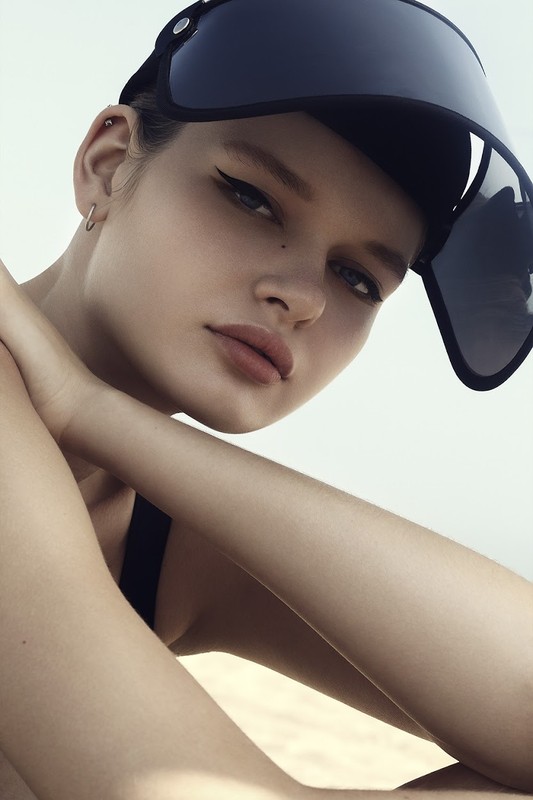 Close-up portrait of a female fashion model wearing a visor hat, showcasing beauty and style with soft, natural lighting.