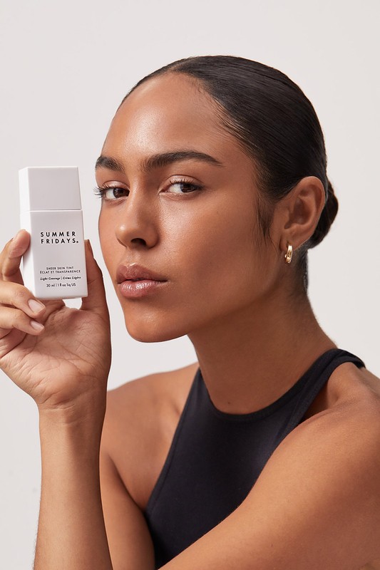 Brunette woman holds Summer Fridays skincare product. Beauty shot in front of a plain background. Fashion, beauty, and skincare theme.