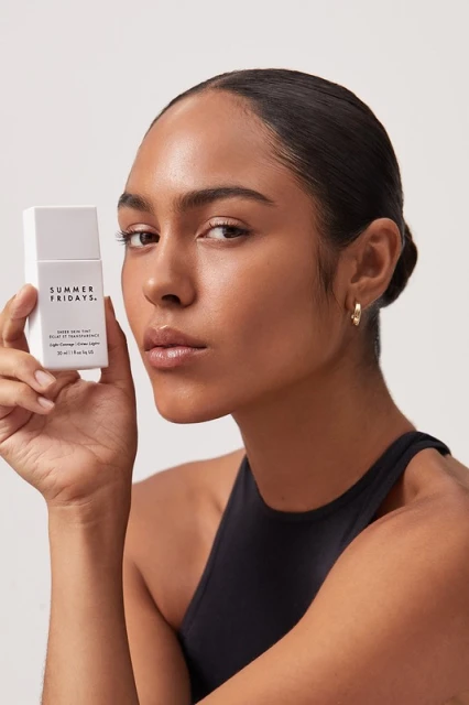 Brunette woman holds Summer Fridays skincare product. Beauty shot in front of a plain background. Fashion, beauty, and skincare theme.