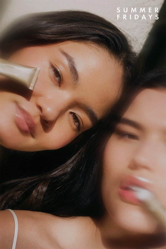 Close-up of two adult females with dark hair, one holding a cosmetic product; soft lighting and shallow depth of field enhance the beauty.