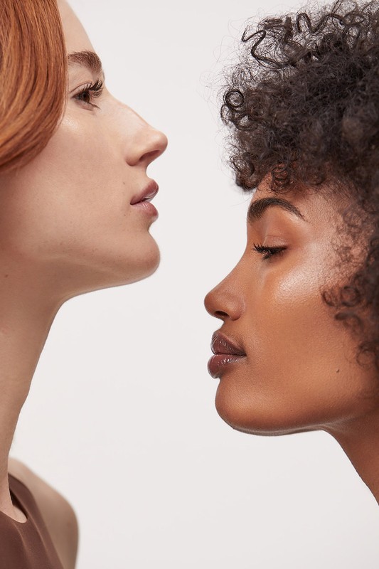 Close-up of two women with different skin tones and hair textures, showcasing diverse beauty against a clean, white background.