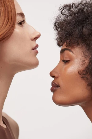 Close-up of two women with different skin tones and hair textures, showcasing diverse beauty against a clean, white background.