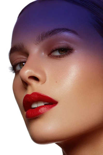 Close-up portrait of a woman with vibrant red lipstick, highlighted cheekbones, and clean skin, against a stark white backdrop.