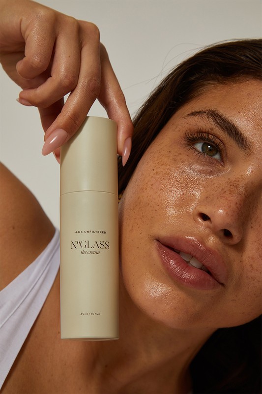 Adult woman poses indoors, holding a skincare product. Close-up shot with focus on the product and her face, showcasing beauty and skincare.