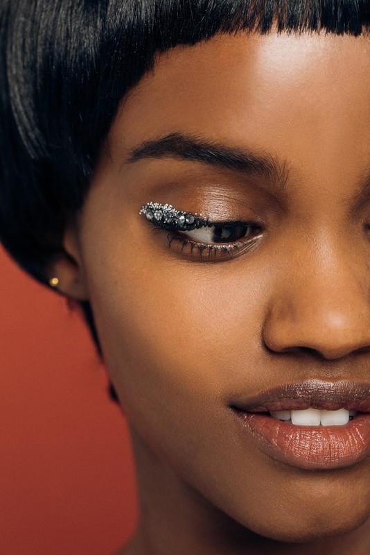 Close-up beauty shot of a Black woman with shiny, sparkling makeup, dark hair, and a red background. Focus on facial features, skin, and textures.