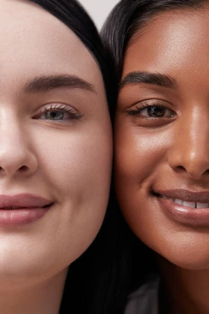Close-up beauty portrait of two smiling women with contrasting fair and dark complexions.