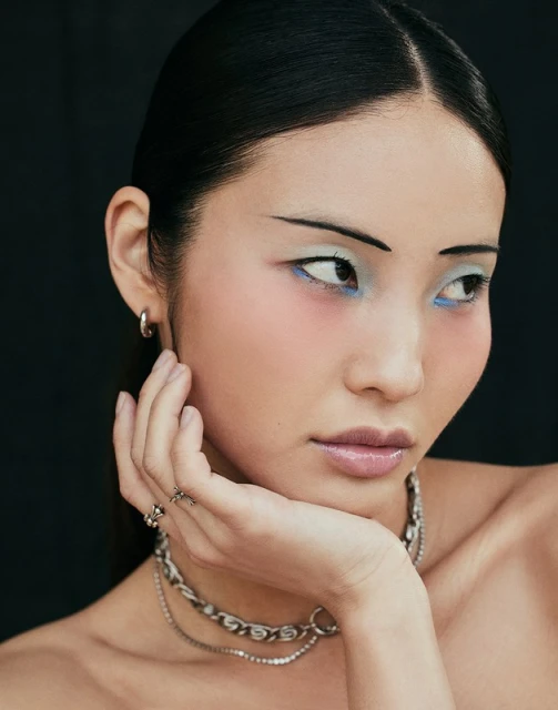 Close-up of an Asian woman with dramatic eye makeup and sleek hair, wearing a silver chain necklace. Fashion and beauty portrait.