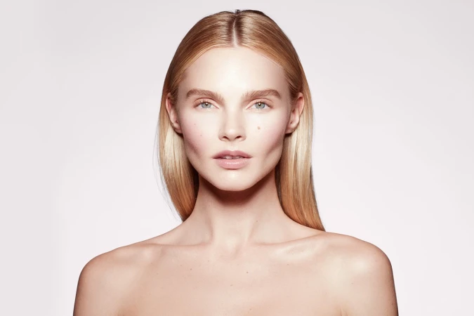 Close-up beauty portrait of a woman with blonde hair and natural makeup against a plain white background