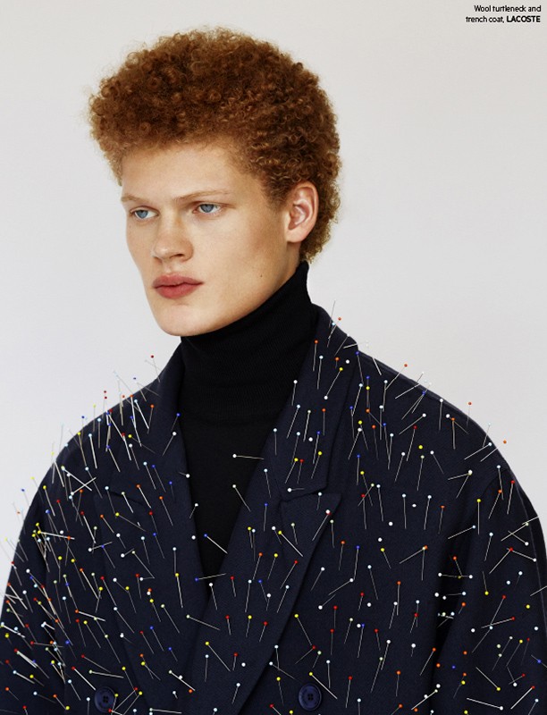 Close-up shot of a male fashion model with an afro wearing a black turtleneck and a dark blue jacket covered in colorful pins.