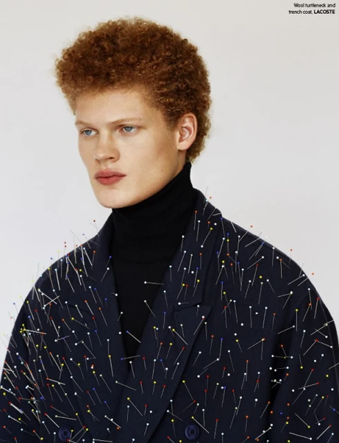 Close-up shot of a male fashion model with an afro wearing a black turtleneck and a dark blue jacket covered in colorful pins.