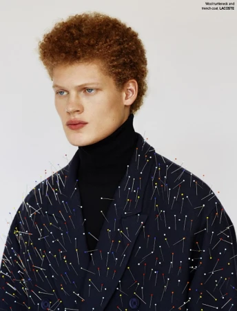 Close-up shot of a male fashion model with an afro wearing a black turtleneck and a dark blue jacket covered in colorful pins.