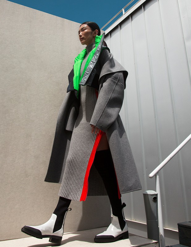 A stylish Asian model poses in an outdoor setting, showcasing a gray wool coat, ribbed dress with thigh-high slit, and white Chelsea boots.