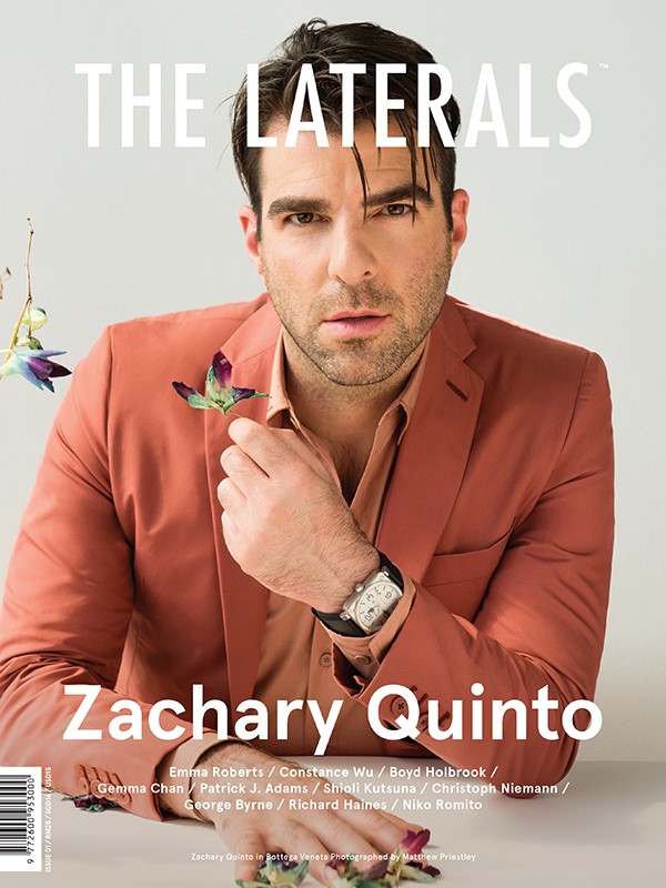 Zachary Quinto magazine cover. The actor wears a coral suit with flower detail, posing in a studio for a portrait shot.
