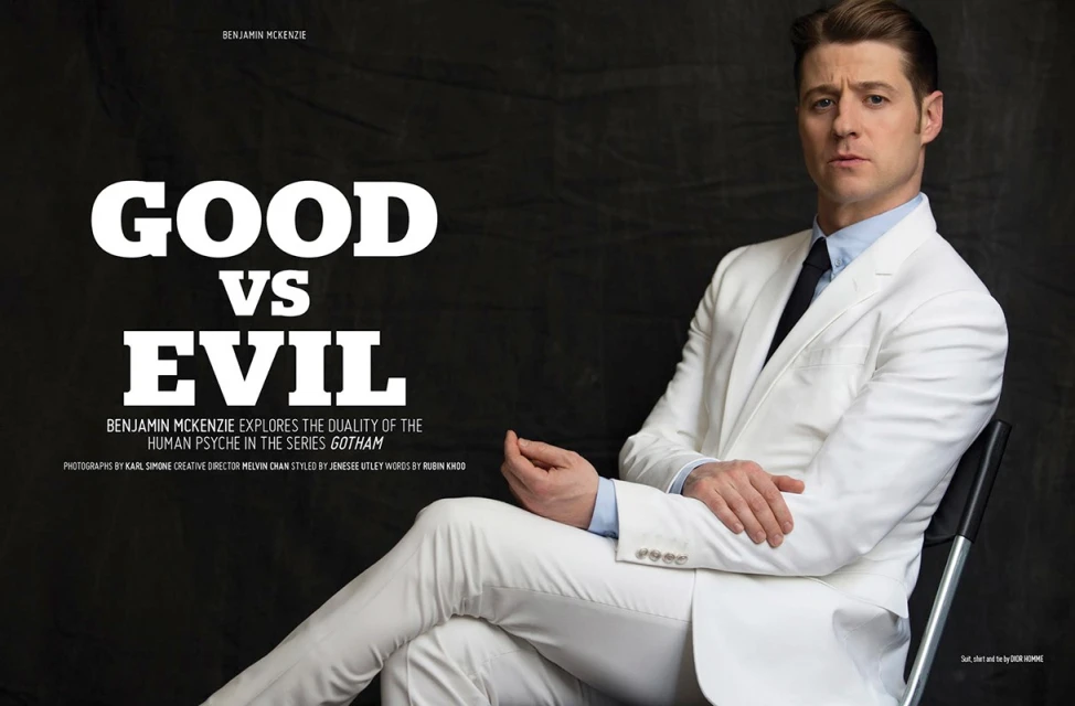 Benjamin McKenzie poses in a white suit against a dark background for a magazine cover promoting the TV series Gotham. 