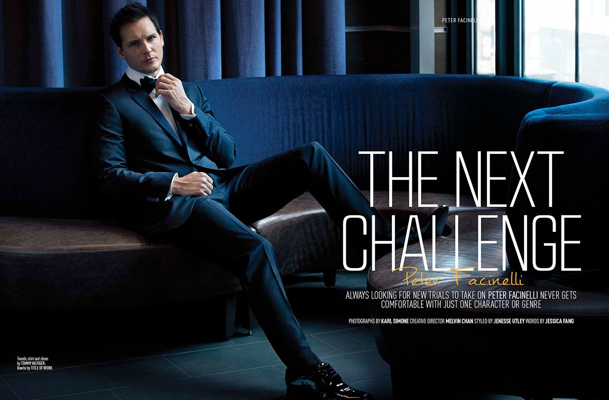 Peter Facinelli poses in a dark suit on a navy couch in a dimly lit room, gazing off-camera, in a celebrity editorial shot.