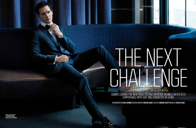 Peter Facinelli poses in a dark suit on a navy couch in a dimly lit room, gazing off-camera, in a celebrity editorial shot.