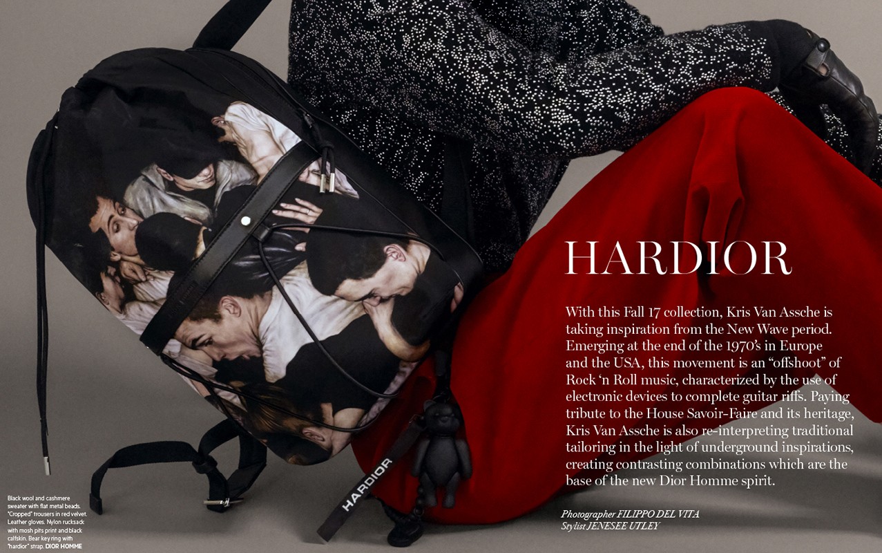 Black backpack with a group of men printed on it, accented by a stylish red trouser and black patterned jacket in a fashion editorial.
