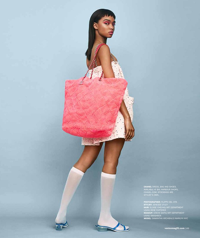 Fashion editorial shot of a young Black woman in a polka dot dress, knee-high socks and sandals, holding a pink quilted tote bag.