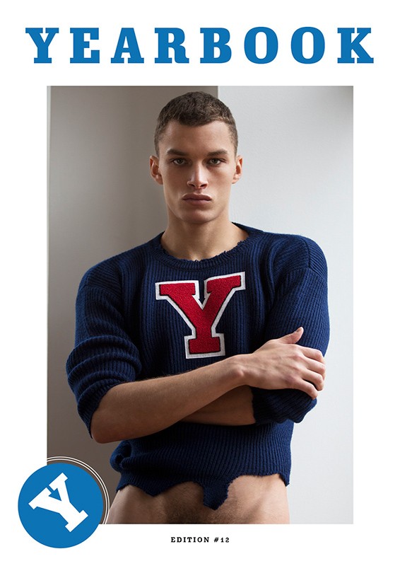 Young man with crossed arms wearing a blue sweater with a red Y emblem styled by Jenesee Utley