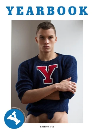 Young man with crossed arms wearing a blue sweater with a red Y emblem styled by Jenesee Utley