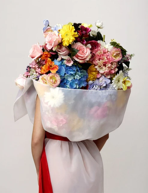 Person from the back wearing a dress with a large bouquet of flowers on their head, set against a plain, neutral background.