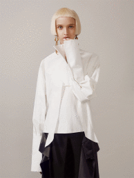 Model with blonde bob wearing a white structured shirt with long cuffs against a neutral background