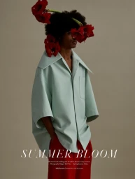 Model with red flowers in afro hairstyle wearing an oversized light blue shirt and red trousers against a neutral background.