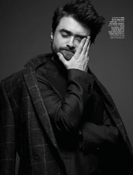 Monochrome portrait of Daniel Radcliffe with hand to face wearing a dark plaid coat styled by Jenesee Utley