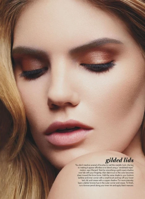 Close-up of a woman's face with closed eyes, featuring bronze eyeshadow, long eyelashes, and soft blonde hair framing her face.