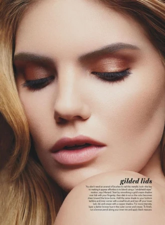 Close-up of a woman's face with closed eyes, featuring bronze eyeshadow, long eyelashes, and soft blonde hair framing her face.