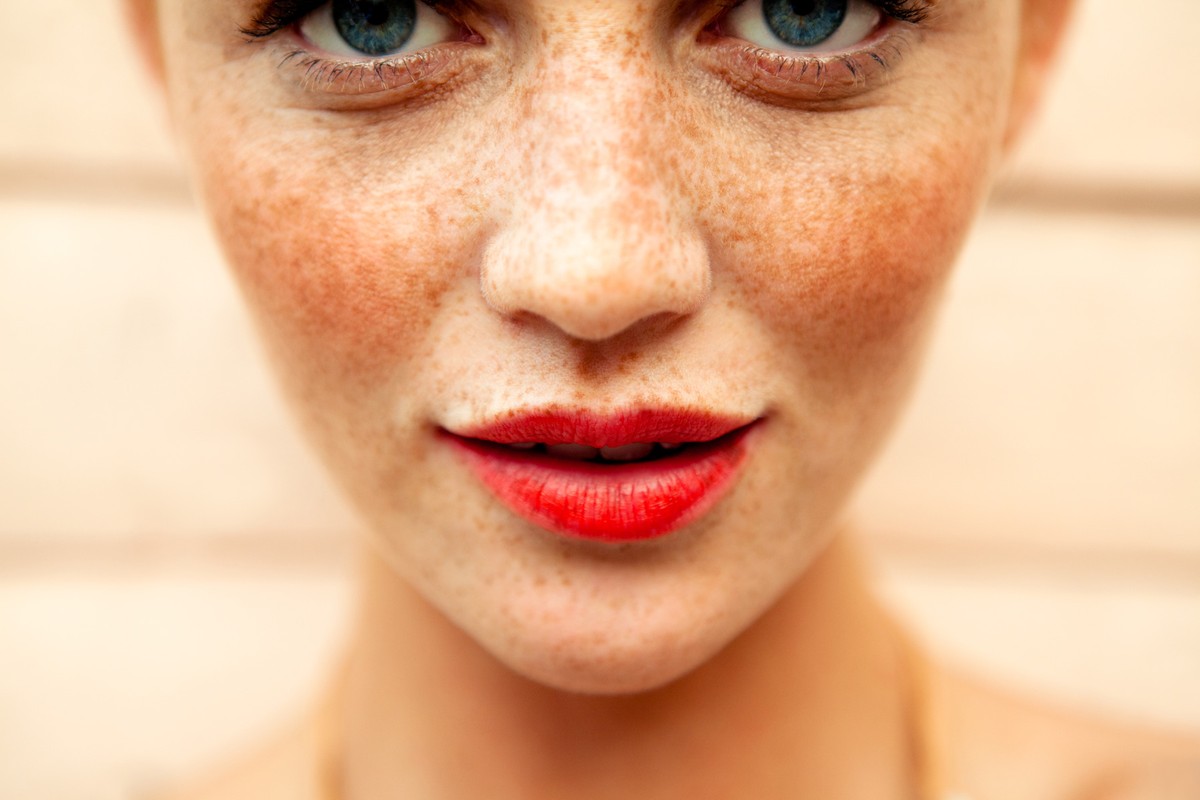 Close-up portrait of a woman with prominent freckles and bright red lipstick by makeup artist Jenna Menard