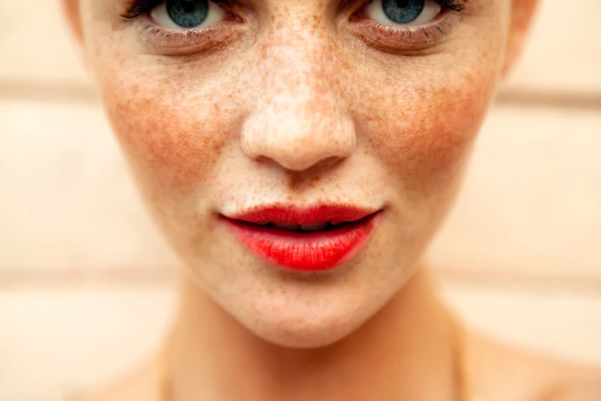 Close-up portrait of a woman with prominent freckles and bright red lipstick by makeup artist Jenna Menard