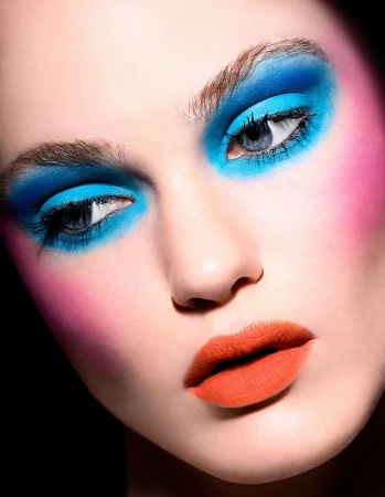 Close-up beauty portrait of a model featuring vibrant blue eyeshadow and bright orange lipstick by Jenna Menard.