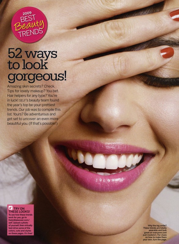Close-up of a smiling woman with bright pink lipstick and red nail polish covering one eye in a beauty trends advertisement.