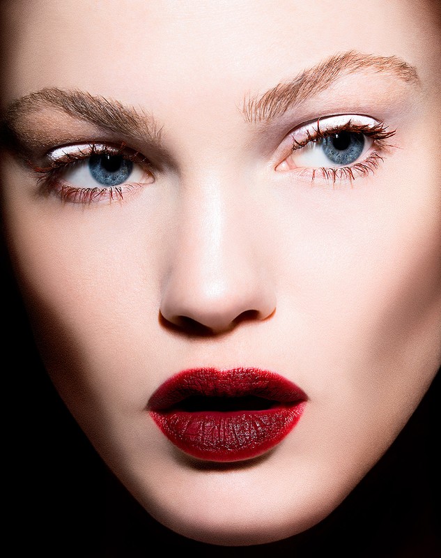 Close-up beauty portrait of a woman with blue eyes, bold dark red lipstick, and white eyeliner by Jenna Menard
