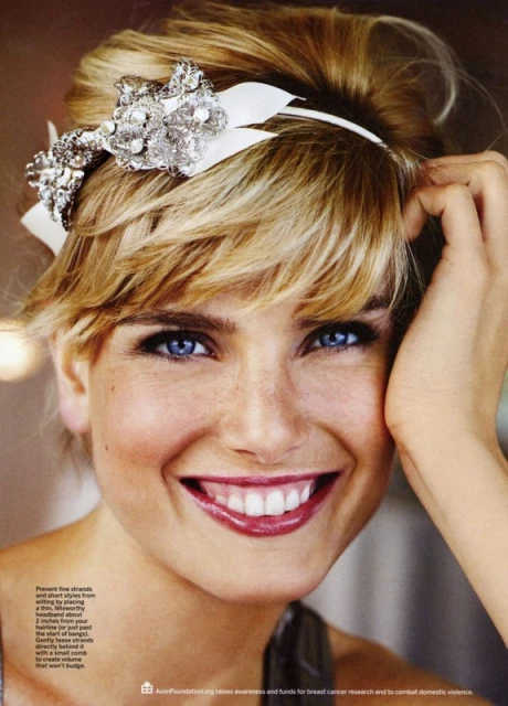 Close-up studio portrait of a smiling, fair-skinned adult woman with bright blue eyes, wearing a decorative hair accessory.