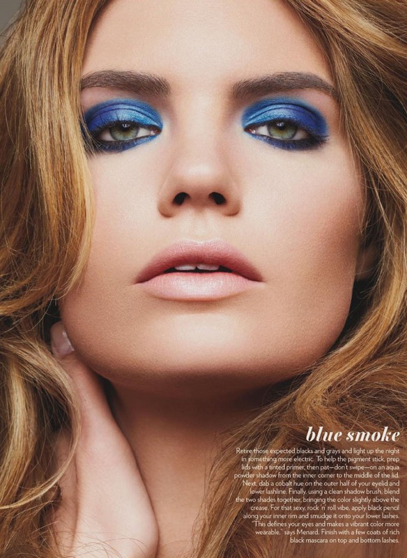 Close-up of a woman's face showcasing vibrant blue eyeshadow and light pink lipstick, with soft brown hair framing her face.