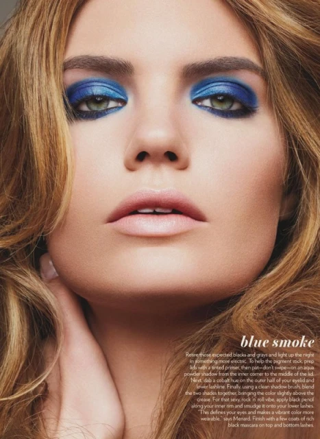 Close-up of a woman's face showcasing vibrant blue eyeshadow and light pink lipstick, with soft brown hair framing her face.