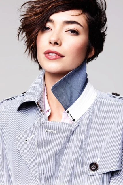 Close-up portrait of a woman with short brown hair and a blue and white striped jacket against a grey background in a photo studio.