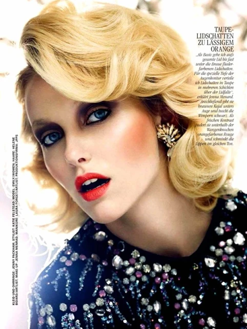 Blonde woman with red lipstick and taupe eyeshadow. She wears a black dress with jewel embellishments and gold earring. Beauty shot.