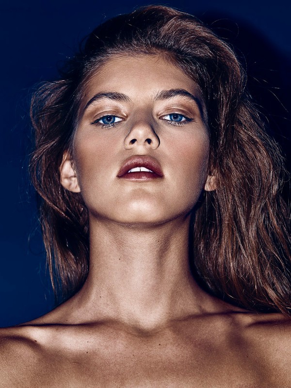 Close-up portrait of a model with dramatic makeup and blue eyes against a dark blue background