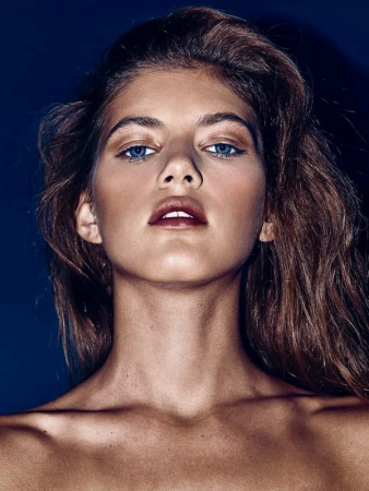 Close-up portrait of a model with dramatic makeup and blue eyes against a dark blue background
