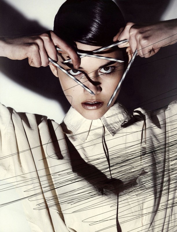 Eye-level shot of a woman in a collared shirt, holding silver sticks in front of her face with sketch lines overlaid on the image.